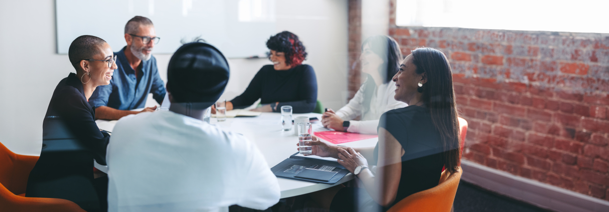 Smiling businesspeople sitting together in a meeting room. Group of successful businesspeople attending their morning briefing in a modern office. Cheerful colleagues working together.